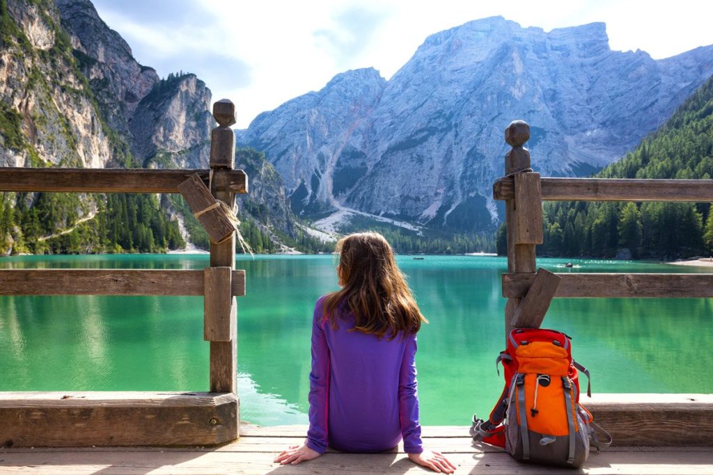 mochilera con su mochila a orillas de un lago en los Dolomitas, Italia