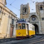 Tranvía amarillo pasando delante de la catedral de Santa María en Lisboa