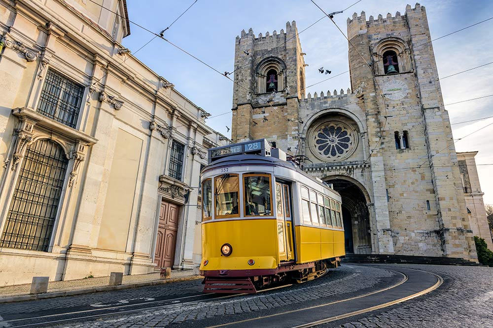 Tranvía amarillo pasando delante de la catedral de Santa María en Lisboa