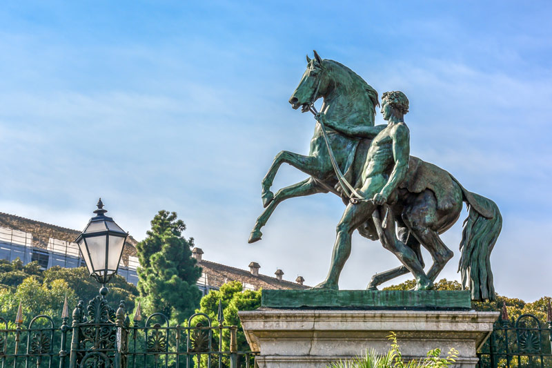 La estatua de bronce del hombre y el caballo frente al jardín del Palacio Real en Nápoles