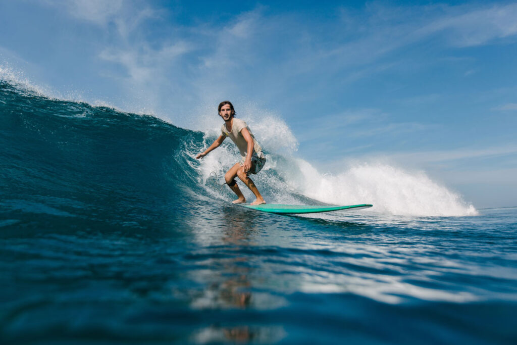 Hombre surfeando una ola en el océano sobre una tabla turquesa, fotografiado desde el nivel del agua