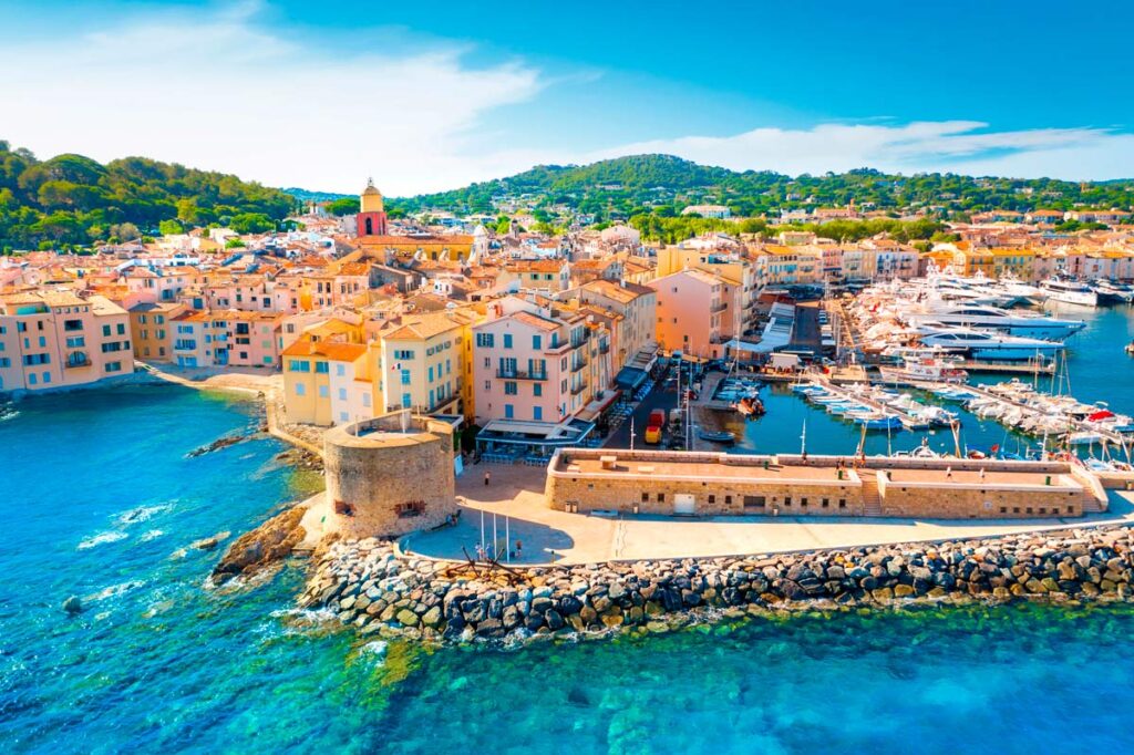 Vista aérea del puerto de Saint-Tropez con edificios de colores pastel, una torre medieval y yates amarrados en aguas turquesas