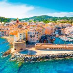 Vista aérea del puerto de Saint-Tropez con edificios de colores pastel, una torre medieval y yates amarrados en aguas turquesas